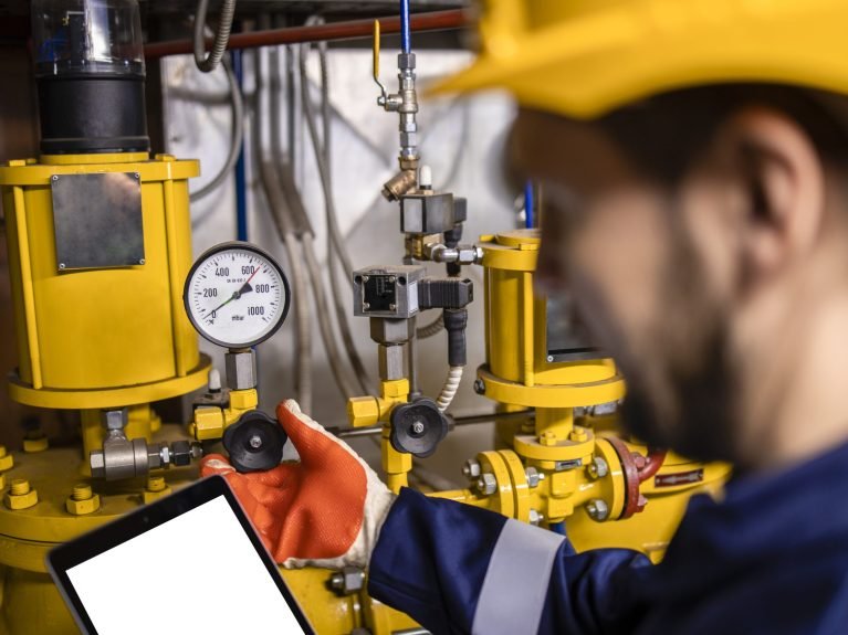 Oil and gas refinery worker measuring pressure of gas pipes and checking tablet computer.