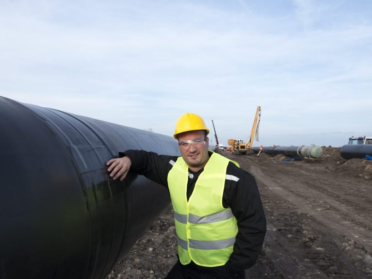 Portrait of an oilfield worker standing by gas pipe at construction site.