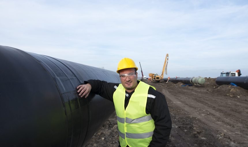 Portrait of an oilfield worker standing by gas pipe at construction site.