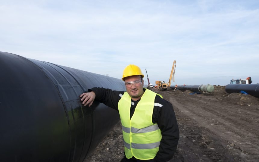 Portrait of an oilfield worker standing by gas pipe at construction site.