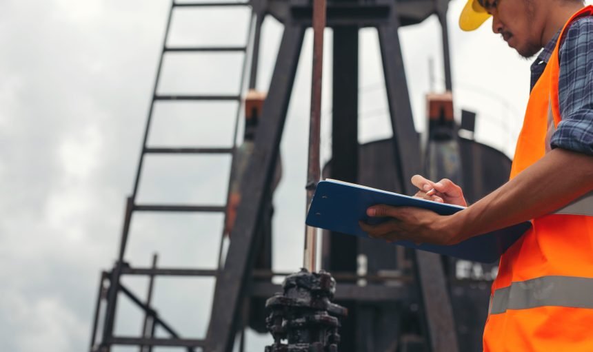 Workers standing and checking beside working oil pumps.