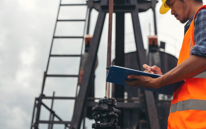 Workers standing and checking beside working oil pumps.
