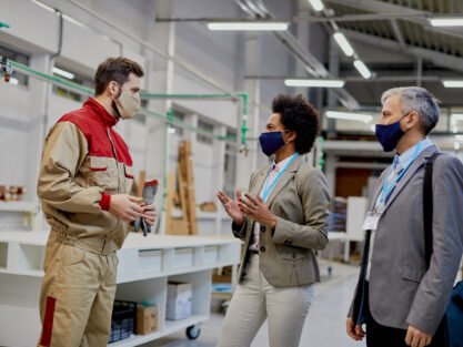 Business people communicating with male worker while visiting woodworking factory during coronavirus pandemic.
