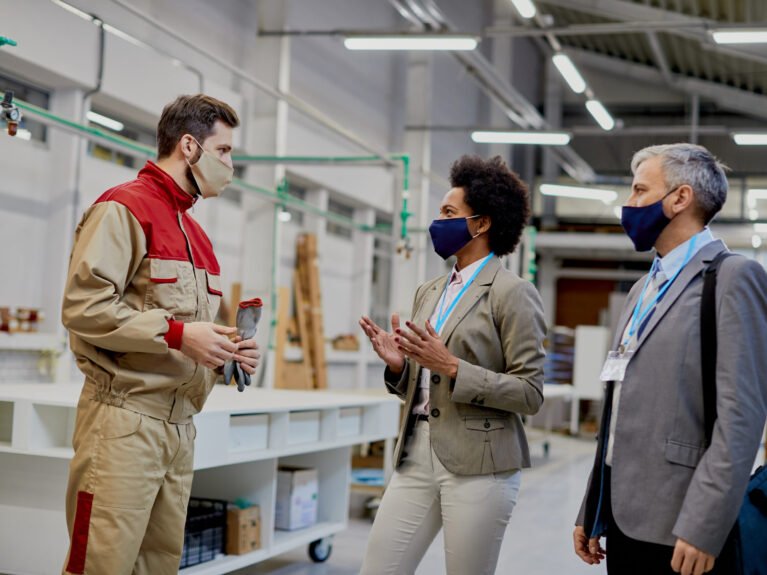 Business people communicating with male worker while visiting woodworking factory during coronavirus pandemic.