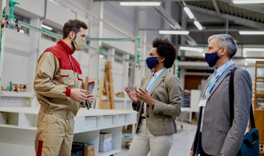 Business people communicating with male worker while visiting woodworking factory during coronavirus pandemic.