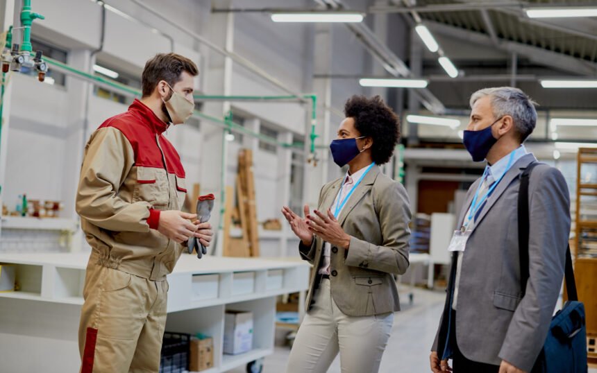 Business people communicating with male worker while visiting woodworking factory during coronavirus pandemic.